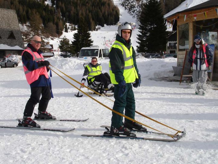 Guide leading disabled skier with tethers attached to the tips of the skis.