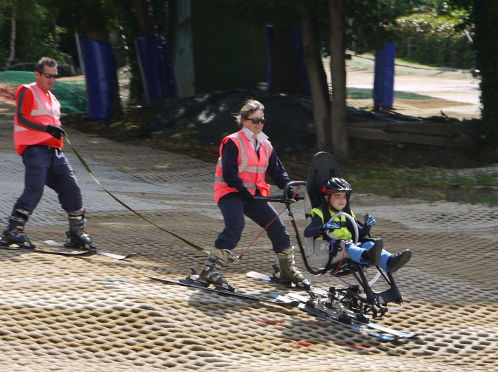 Boy in a sit-ski at a Monthly Session, with 2 Guides aiding him.