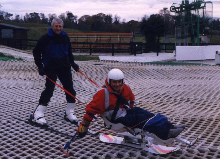 Man in sit-ski with Guide helping him.